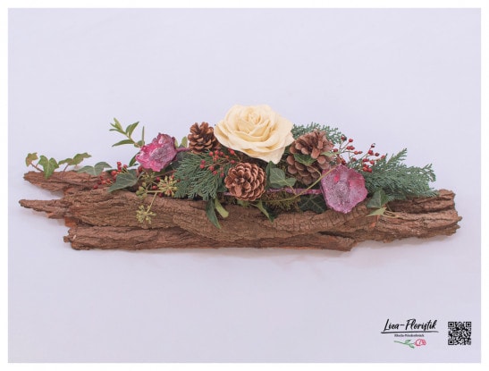 Gesteck auf einer Baumrinde mit Wachsrose, Trockenblumen, Efeu, Zypresse, Gaultheria und Zapfen