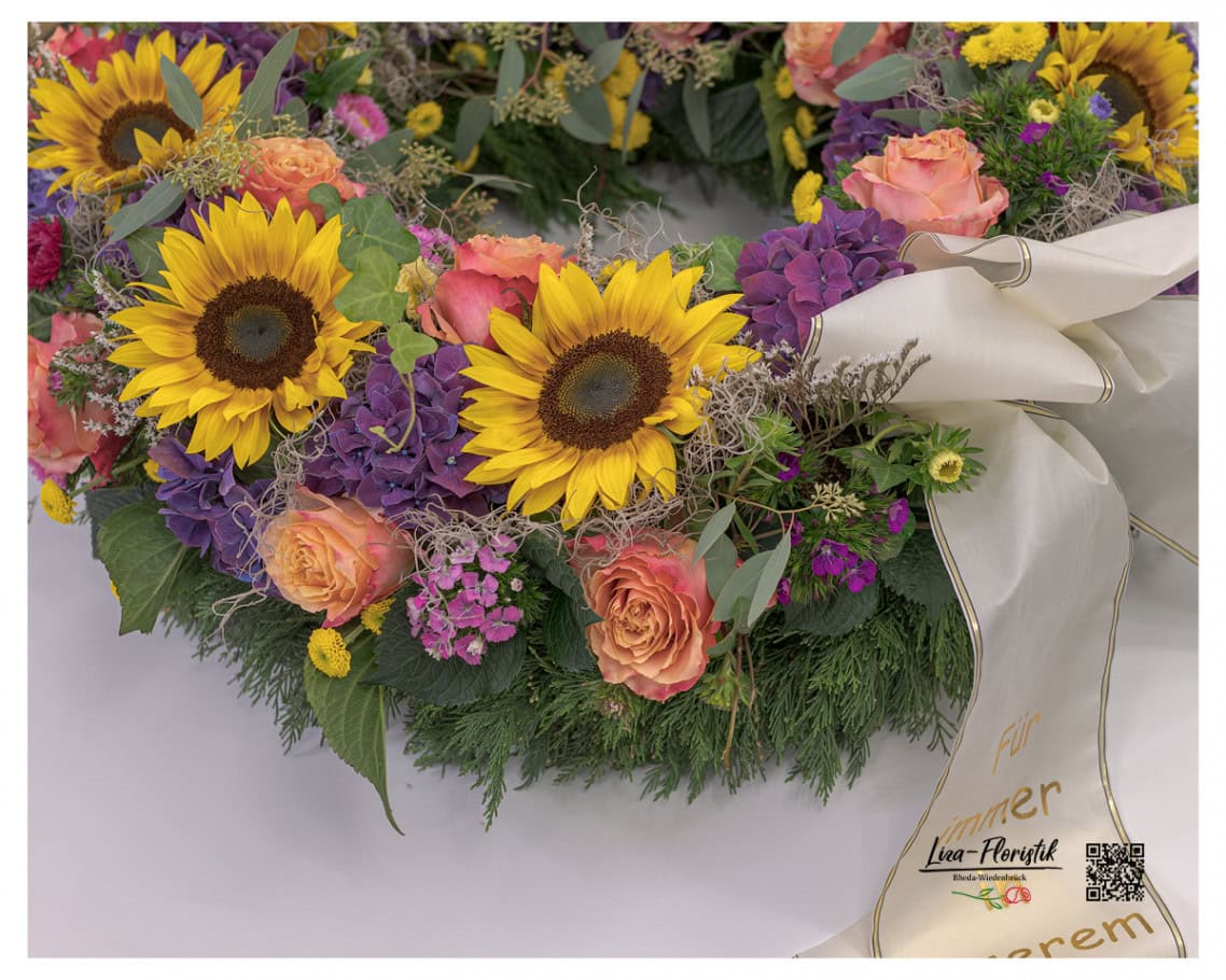 Dieses Detailbild zeigt die prachtvolle Kombination aus leuchtenden Sonnenblumen, violetten Hortensien und apricotfarbenen Rosen, liebevoll ergänzt durch zarte Tillandsia und Santini.