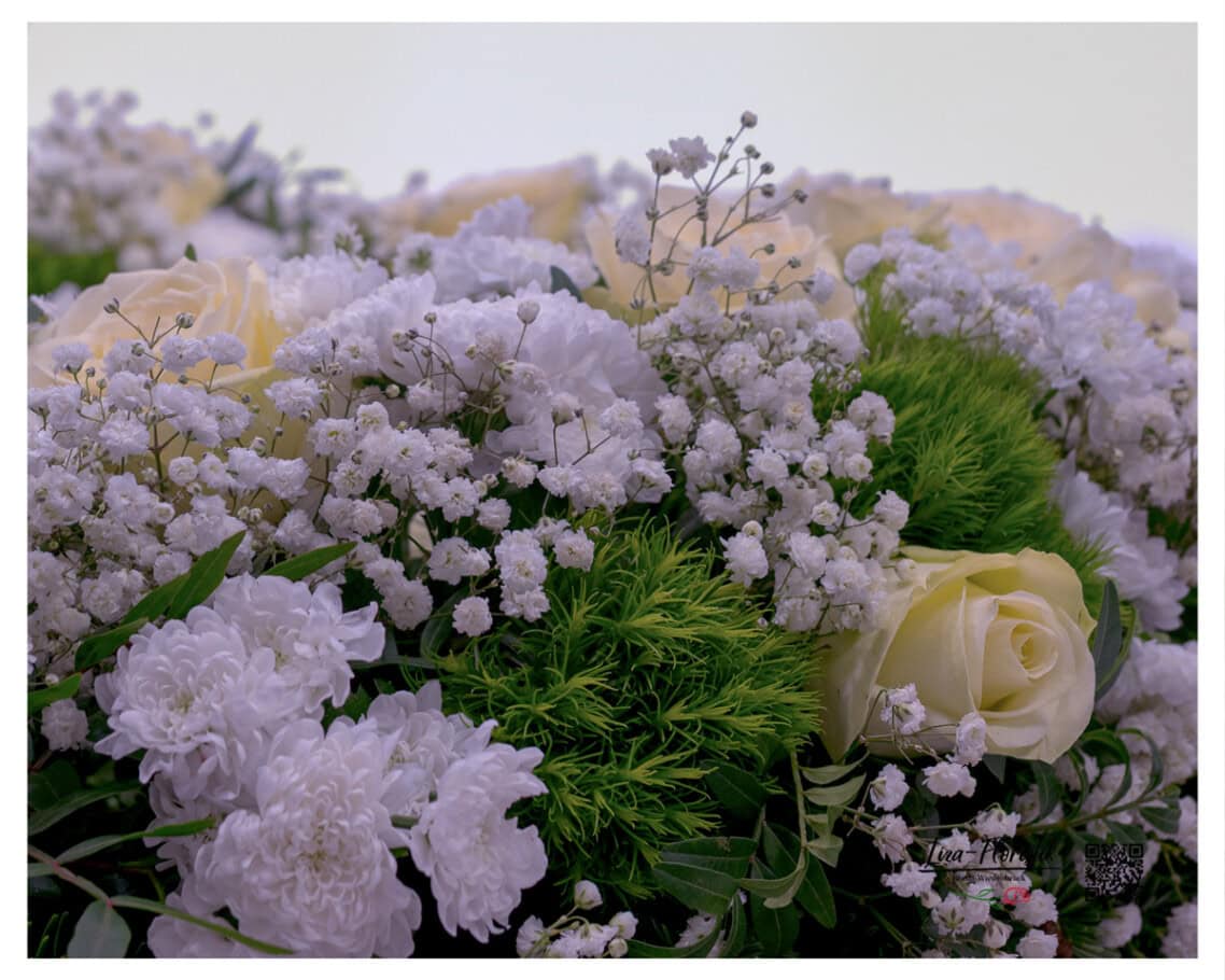 Im Nahblick zeigt sich, wie Schleierkraut und Chrysanthemen die cremefarbenen Rosenblüten rahmen – die Reinheit der weißen Töne gibt dem Kranz seine stille, würdevolle Wirkung