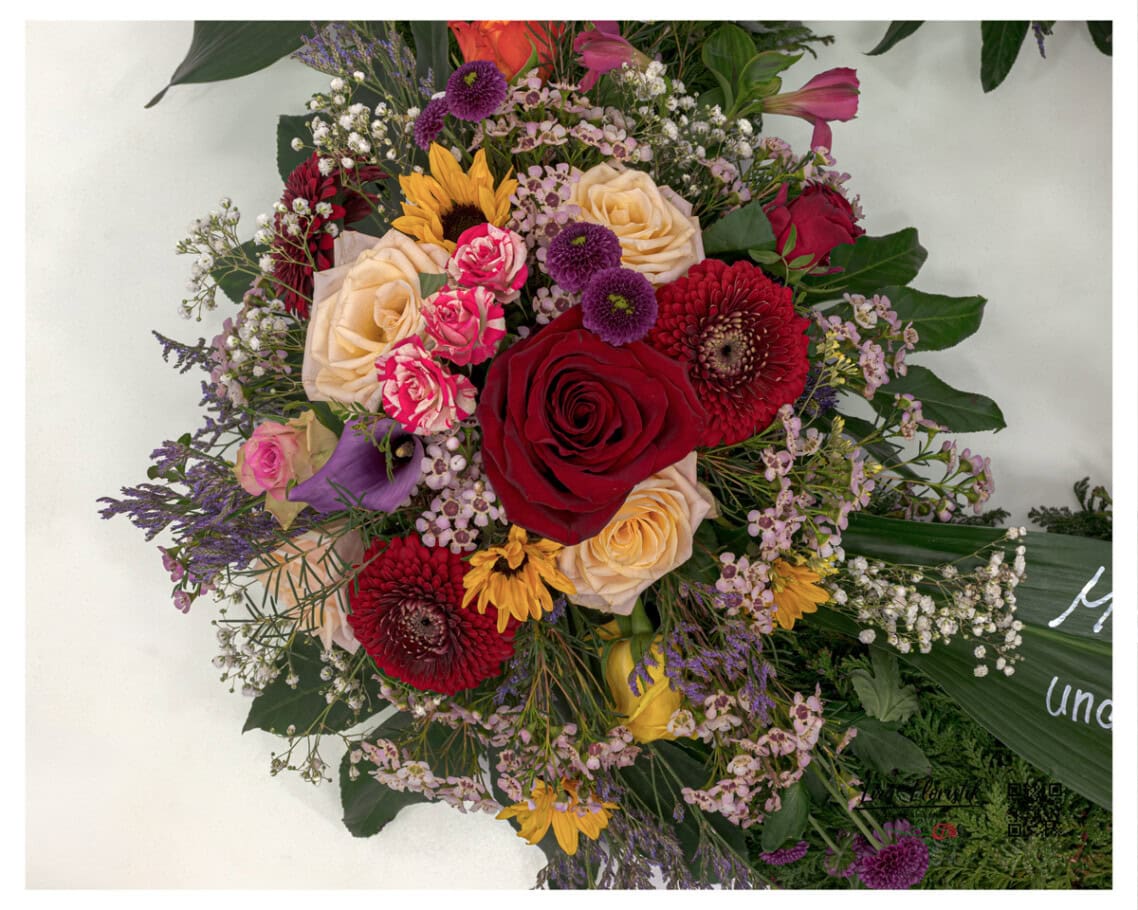 Gesteckpunkt von oben – Premium Rosen, Gerbera, Santini und Waxflower im Trauerkranz
