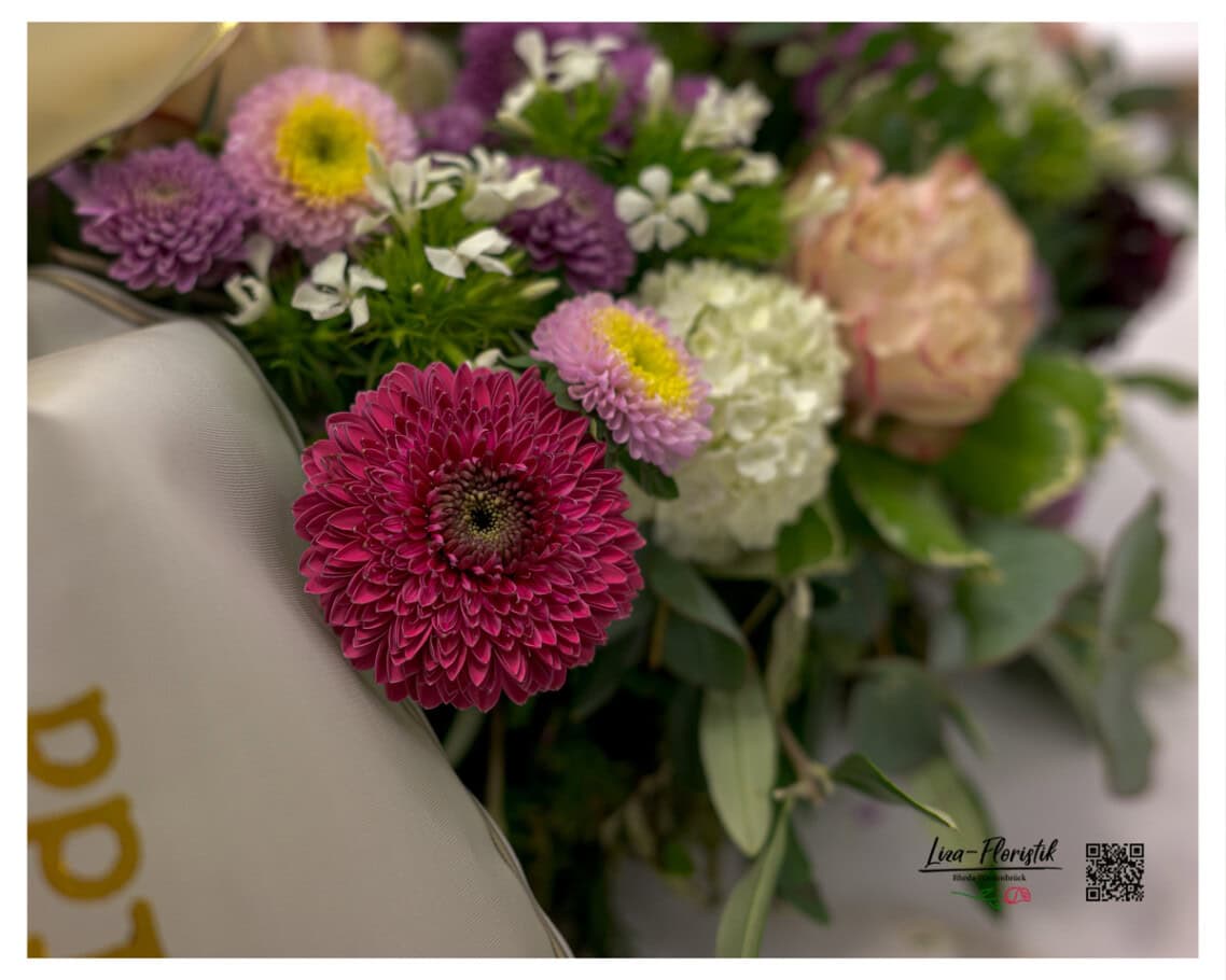 Detailaufnahme: Dunkelrote Gerbera im Vordergrund, umgeben von lila Astern, weißen Bartnelken und einer zartrosafarbenen Rose – sichtbare Handarbeit und sorgfältige Blütenauswahl